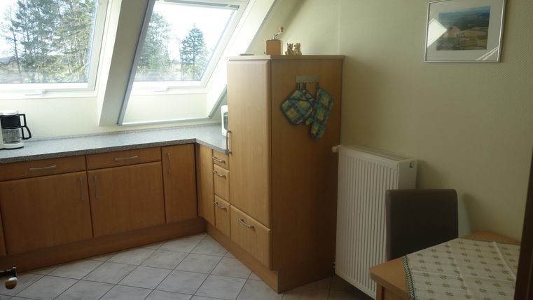 Een lichte keuken met houten kasten en ramen die veel licht binnenlaten. Een tafel en een stoel zijn in de hoek geplaatst.