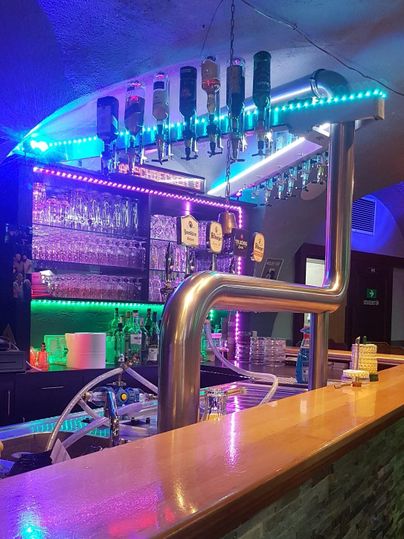Een moderne bar met kleurrijke lichten en een selectie van dranken. De bar is van hout met stijlvolle details.