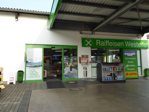 A business entrance with large windows and green accents. There is a selection of snacks and drinks as well as a lottery acceptance point.