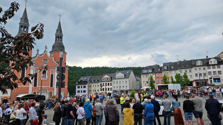 Een druk plein met een kerk op de achtergrond en veel mensen. De lucht is bewolkt en de sfeer is feestelijk.