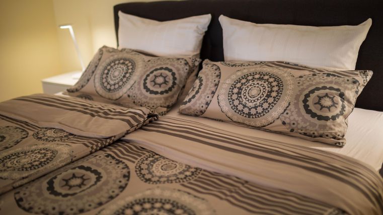 Ein gemütliches Bett mit dekorativen Kissen und einer einem gemusterten Bettdecke. Die ruhigen Farben schaffen eine entspannte Atmosphäre im Schlafzimmer.