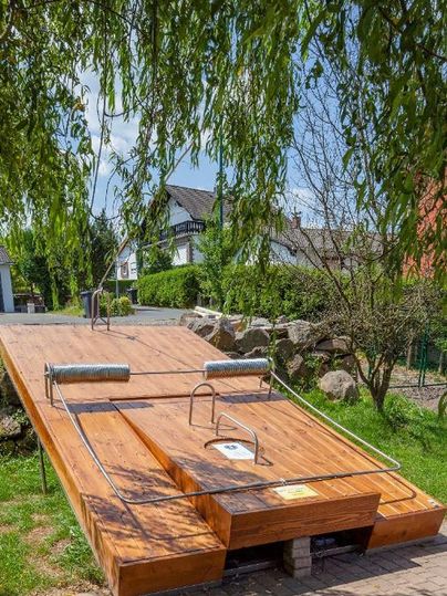 Eine Holzplattform mit einem Zugang zum Wasser und einem Handlauf. Umgeben von Bäumen und Grünflächen.