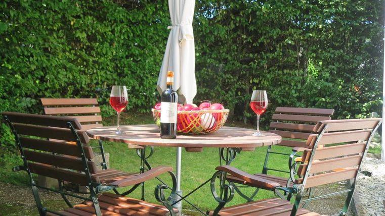 Een uitnodigende tafel in de buitenlucht met vier stoelen. Op de tafel staan twee glazen wijn, een fles wijn en een schaal met appels.