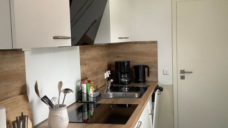 Eine moderne Küche mit weißen Schränken und einer Holzarbeitsplatte. Auf der Arbeitsfläche befinden sich Kochutensilien und eine Kaffeemaschine.