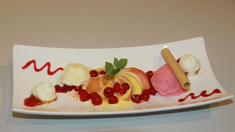 An elegant dessert with various ice cream flavors, fresh fruits, and a decorative sauce. Arranged on a curved plate, garnished with a mint leaf.
