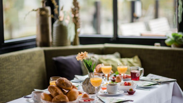 Ein liebevoll gedeckter Tisch mit frischem Gebäck, Säften und Obst. Die Atmosphäre ist gemütlich mit einer schönen Aussicht.