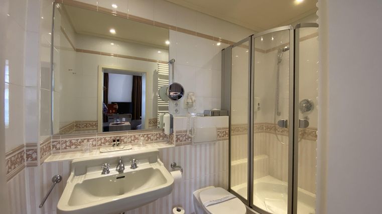 Ein modernes Badezimmer mit einer Dusche, einem Waschbecken und einer Toilette. Die Wände sind hell gefliest und gut beleuchtet.