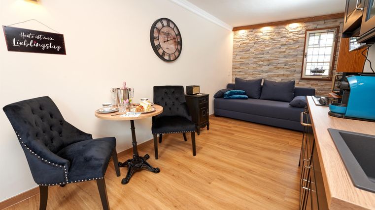 A cozy living room with modern furniture and hardwood flooring. On a small table, there is tea service and two chairs.