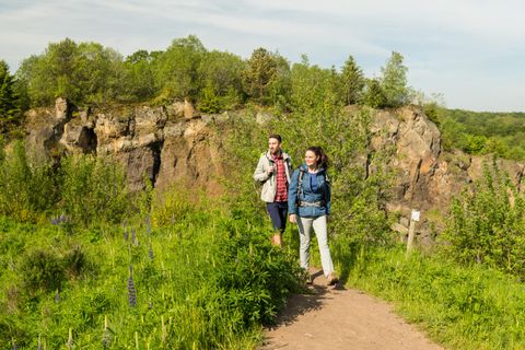 Zwei Wanderer auf einem Pfad im Vulkangarten Steffeln, umgeben von grüner Vegetation und Felsen.
