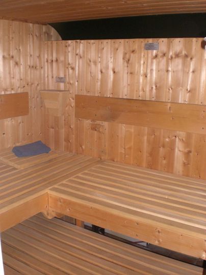 Ein Holzsaunaraum mit Bänken und einer ruhigen, entspannenden Atmosphäre. Die Wände sind aus hellem Holz und es liegt ein Handtuch auf der Bank.