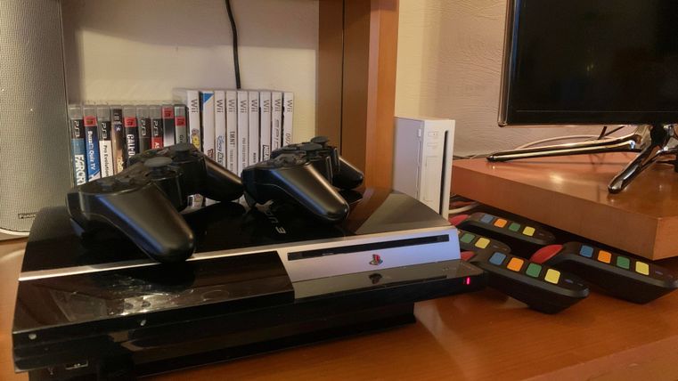 A game console with two controllers is on a shelf. Next to it are game CDs and a remote control.