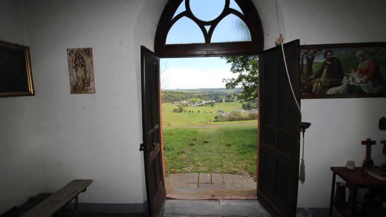 Eine offene Tür mit einem Blick auf eine grüne Landschaft. Im Hintergrund ist ein klarer Himmel und einige Bäume zu sehen.
