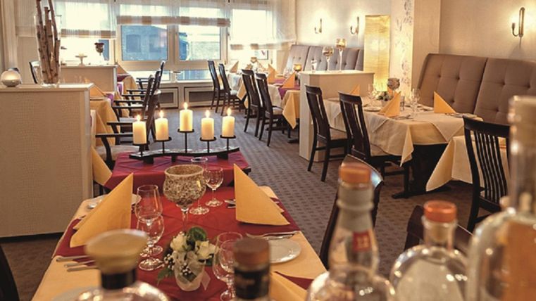 Ein elegantes Restaurant mit gemütlicher Atmosphäre. Tische sind mit roten und gelben Tischdecken sowie Kerzen dekoriert.
