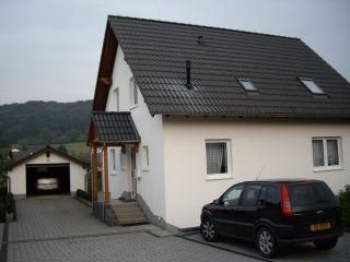 Een modern huis met een grijs dak en een oprit. Voor staat een zwarte auto en op de achtergrond is een garage te zien.