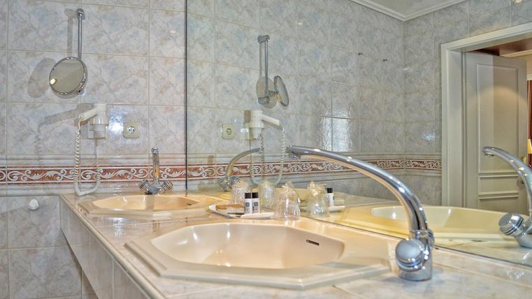 Ein modernes Badezimmer mit zwei Waschbecken und einem großen Spiegel. Die Wände sind hell gefliest und mit dekorativen Elementen verziert.