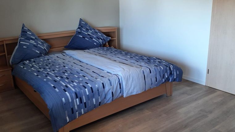 Ein gemütliches Schlafzimmer mit einem großen Bett und modernen Kissen. Der Boden ist aus Holz und die Wände sind in neutralen Farben gehalten.