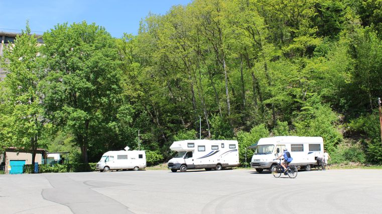 Ein Campingplatz mit mehreren Wohnmobilen und viel grünem Laub. Ein Radfahrer fährt auf dem Weg vorbei.
