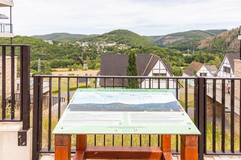 Eine Aussichtsplattfom mit einem Informationsschild, das die Umgebung beschreibt. Im Hintergrund sind grüne Hügel und typische deutsche Häuser zu sehen.