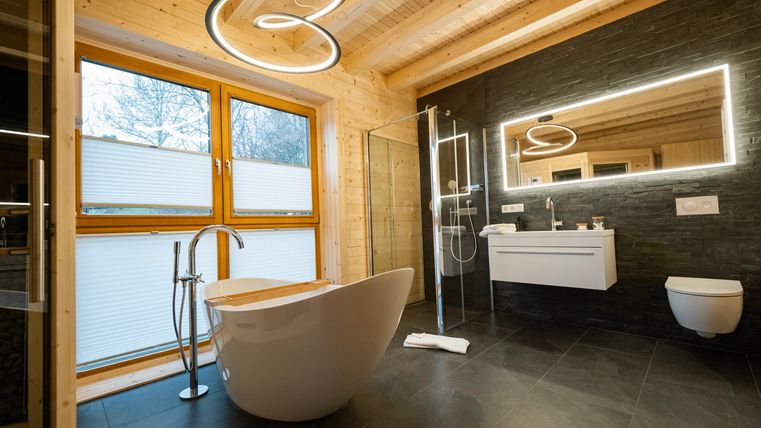 Ein modernes Badezimmer mit einer freistehenden Badewanne und einer geräumigen Dusche. Große Fenster sorgen für viel Tageslicht und eine einladende Atmosphäre.