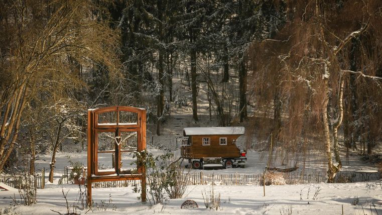 Een mooi houten huis staat in een besneeuwd landschap omringd door bomen. In de voorgrond is een rustieke houten hek met een vensterinstallatie te zien.