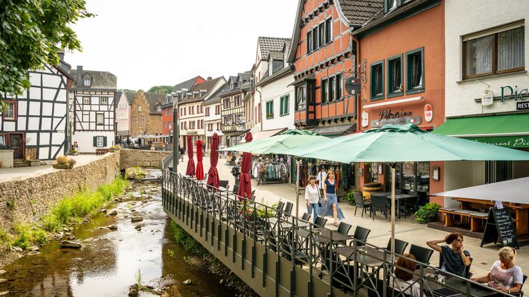 Eine malerische Flusslandschaft mit Cafés an der Uferpromenade. Historische Gebäude umgeben die Szene, die eine entspannte Atmosphäre ausstrahlt.