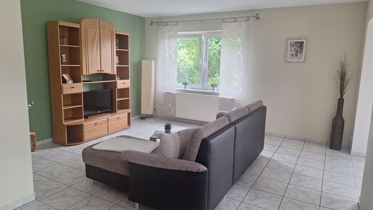 Ein modernes Wohnzimmer mit einem großen, bequemen Sofa und einem Fernsehmöbel. Der Raum hat eine helle, freundliche Atmosphäre mit einem Fenster, das Blick nach draußen bietet.