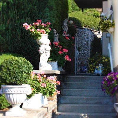 Ein schöner Eingang mit blühenden Pflanzen und Skulpturen. Die Treppe führt zu einem verzierten Tor.