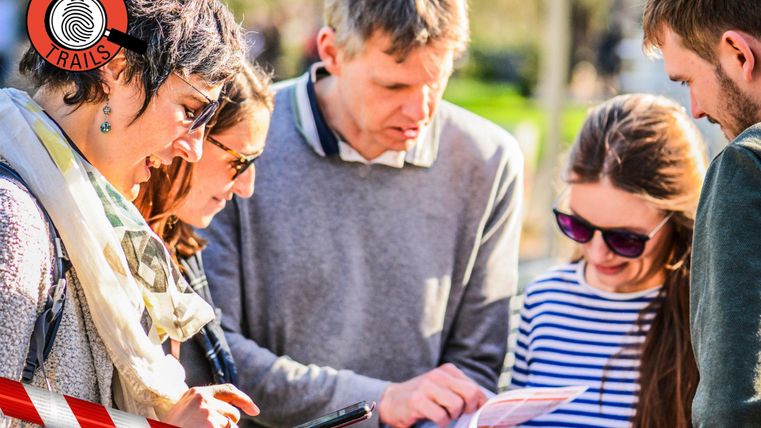Eine Gruppe von fünf Personen steht im Freien und studiert eine Karte. Sie scheinen an einer Erkundungstour teilzunehmen.