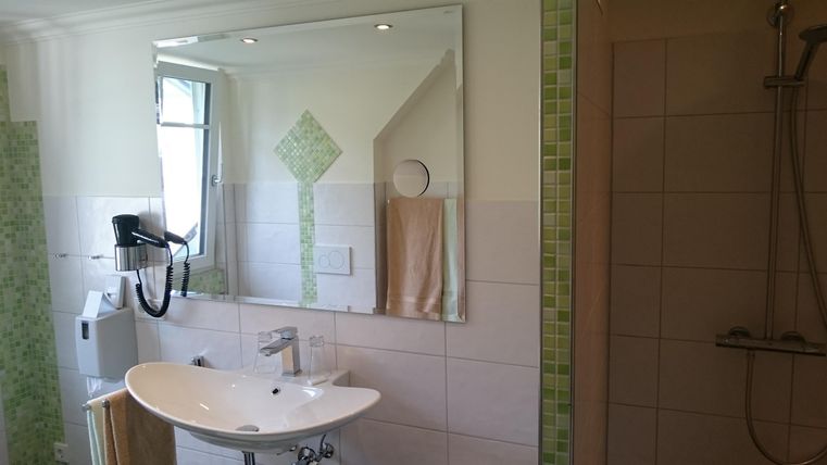 Ein modernes Badezimmer mit hellen Fliesen und einem großen Spiegel. Der schlichte Waschbeckenbereich ist mit einem Handtuch und einer Dusche ausgestattet.