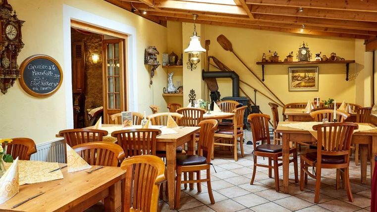 Ein gemütliches Restaurant mit Holztischen und -stühlen. Die warme Atmosphäre wird durch natürliches Licht und eine rustikale Einrichtung unterstrichen.