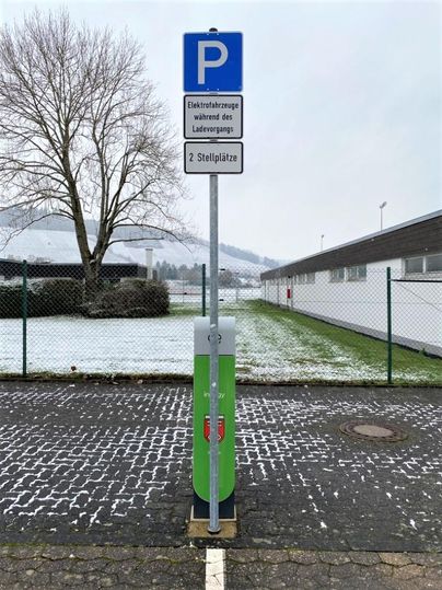 Ein Parkplatz für Elektrofahrzeuge mit zwei Stellplätzen. Im Hintergrund sind Schnee und Bäume zu sehen.