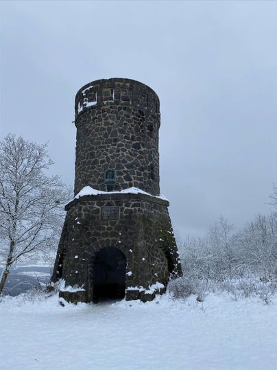 Ein alter Steinturm in einer verschneiten Landschaft. Der Himmel ist grau und die Umgebung ist mit Schnee bedeckt.