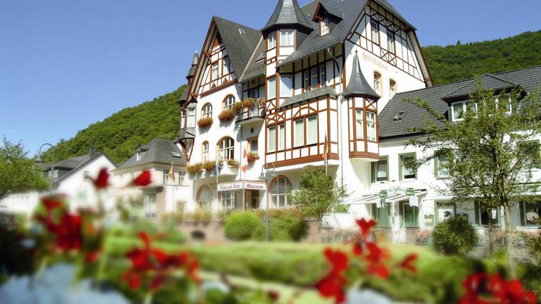 Ein schönes, traditionelles Gebäude mit Fachwerk-Architektur. Im Vordergrund blühen bunte Blumen in einem gepflegten Garten.