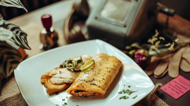 A plate with two savory omelets, garnished with spring onions and lime slices. In the background, kitchen utensils and plants can be seen.