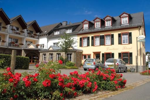 Ein einladendes Gasthaus mit blühenden roten Rosen im Vordergrund. Es gibt helle Gebäude und einen klaren blauen Himmel.