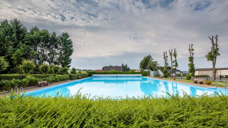 Ein klarer Pool umgeben von grünen Pflanzen und Bäumen. Der Himmel ist leicht bewölkt und bietet eine ruhige Atmosphäre.