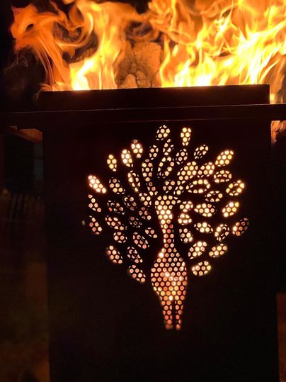 Eine dekorative Feuerstelle mit einem kunstvollen Pfau-Muster. Flammen lodern im Hintergrund und schaffen eine warme Atmosphäre.