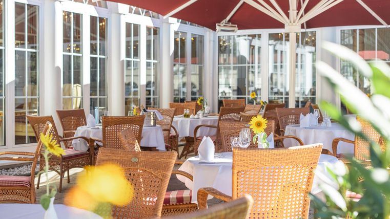 Een gezellige restaurantomgeving met mooi gedekte tafels. De sfeer is licht en uitnodigend, omringd door planten en parasols.