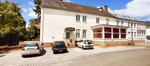 A building with several windows and a covered area. In the foreground, several cars are parked in a parking lot.
