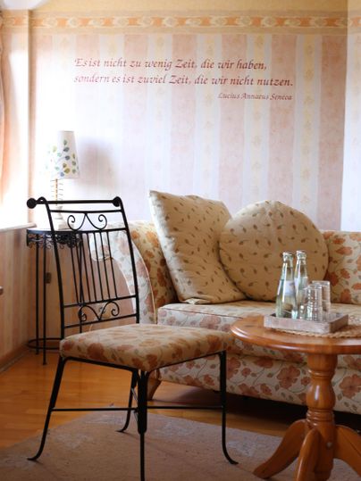 Ein gemütliches Wohnzimmer mit einer beigen Couch und einem Tisch aus Holz. Auf der Wand steht ein inspirierendes Zitat.