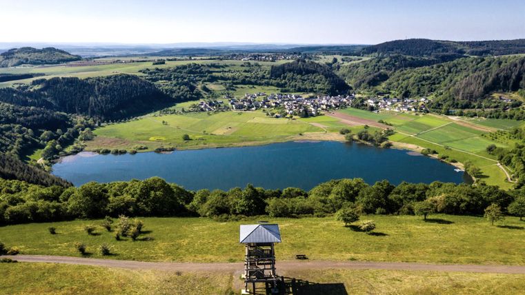 Een schilderachtig landschap met een helder meer en weelderige bossen. Op de voorgrond staat een uitkijktoren die een prachtig uitzicht op de omgeving biedt.