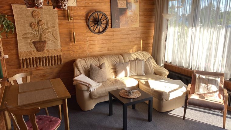 Ein gemütlicher Wohnraum mit Holzverkleidung, einer Couch und einem Tisch. Große Fenster lassen viel Licht herein und schaffen eine einladende Atmosphäre.