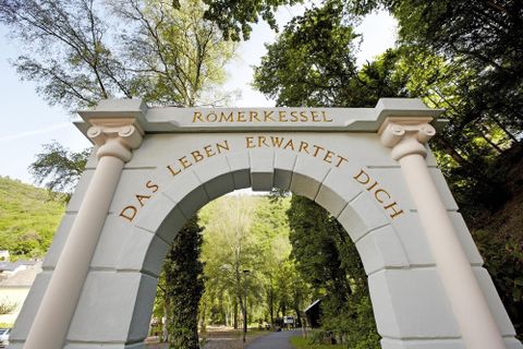 A beautiful archway with the inscription "Roman Cauldron" and "Life Awaits You". Surrounded by green trees and a picturesque landscape.