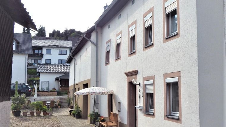 A quiet inner courtyard with two buildings. On the right side, there is a table with a sunshade and some plants are visible.