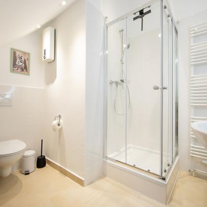 Een moderne badkamer met een glazen douche, een wastafel en een toilet. De wanden zijn licht en de ruimte oogt schoon en vriendelijk.