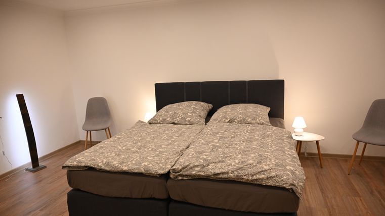 Een gezellige slaapkamer met een tweepersoonsbed en moderne stoelen. De muren zijn neutraal, en er is een aangename verlichting.