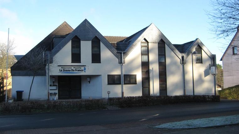 A modern building with a pointed roof and the inscription 'Ristorante Pizzeria La Sirena Da Franco' on the facade.