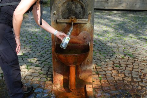 Ein Wasserbrunnen mit Rost, aus dem frisches Wasser fließt. Eine Person füllt eine Flasche mit Wasser.
