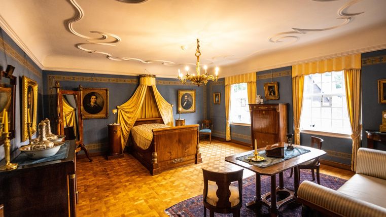 Een stijlvolle kamer met een groot bed en elegante inrichting. De muren zijn versierd met historische afbeeldingen en het licht is warm en uitnodigend.