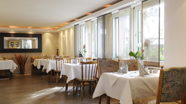 Ein elegantes Restaurant mit Tischdecken und Holzstühlen. Große Fenster sorgen für viel Tageslicht und eine angenehme Atmosphäre.